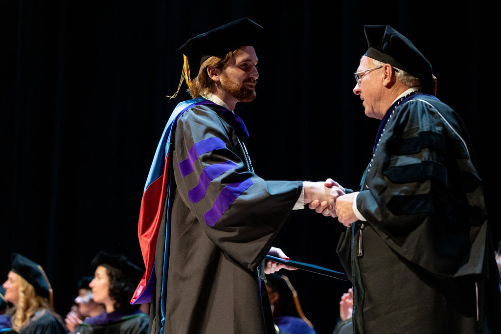 Photo of a student graduating and shaking hands with Professor Chapman on the stage.