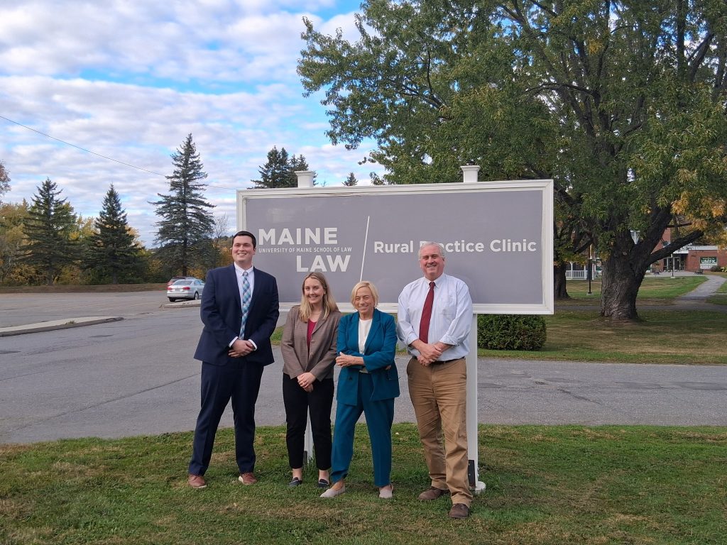 A photo of four individuals standing in front of a sign that reads "Rural Practice Clinic.