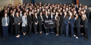 A photo of the Class of 2029 taken in the Moot Courtroom, students out front hold a Maine Law flag.