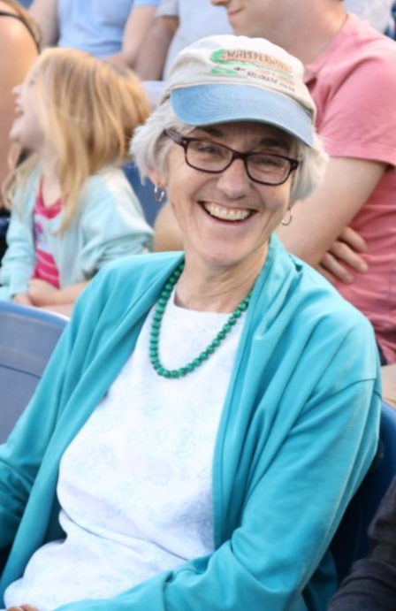 Wriggins wearing a baseball hat and smiling at the camera at a baseball stadium.